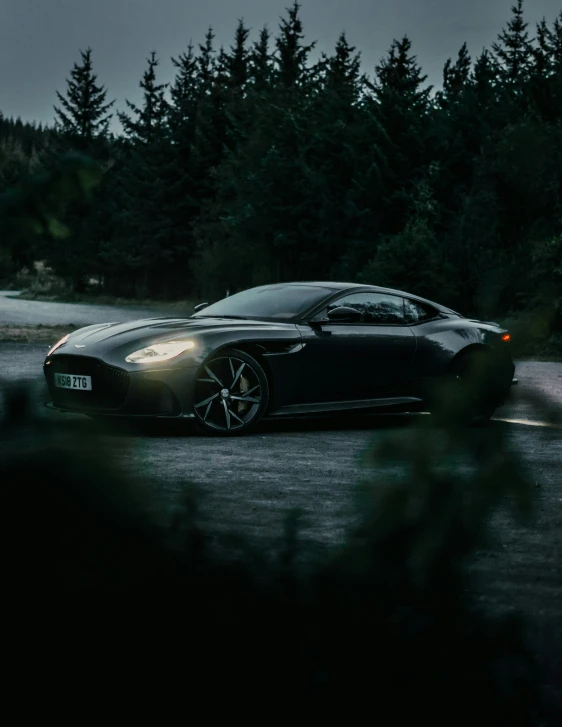 a dark car is parked in front of some trees