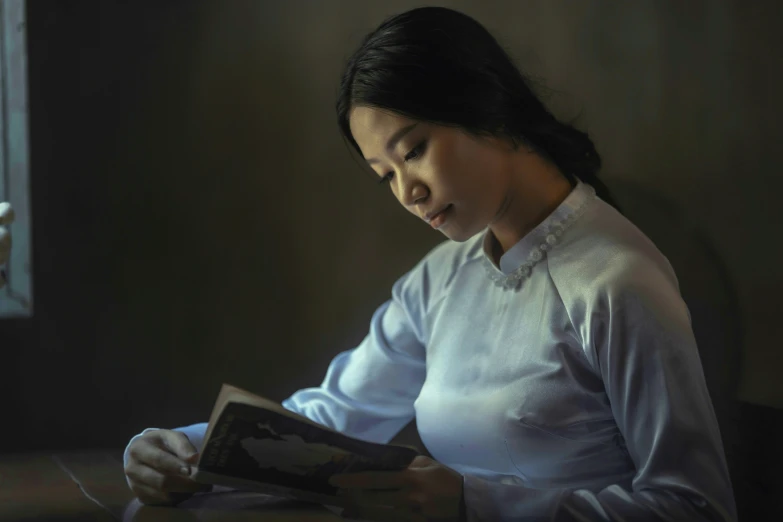 woman reading a book while sitting at table in dark room