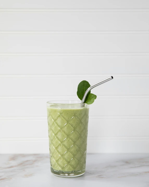 a tall glass with a drink on the rim with a green leaf sticking out