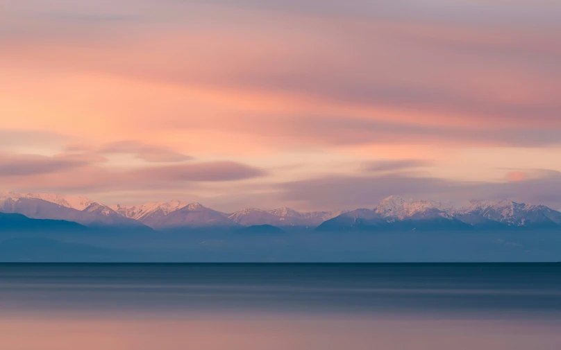 the clouds gather over the mountain tops near a body of water