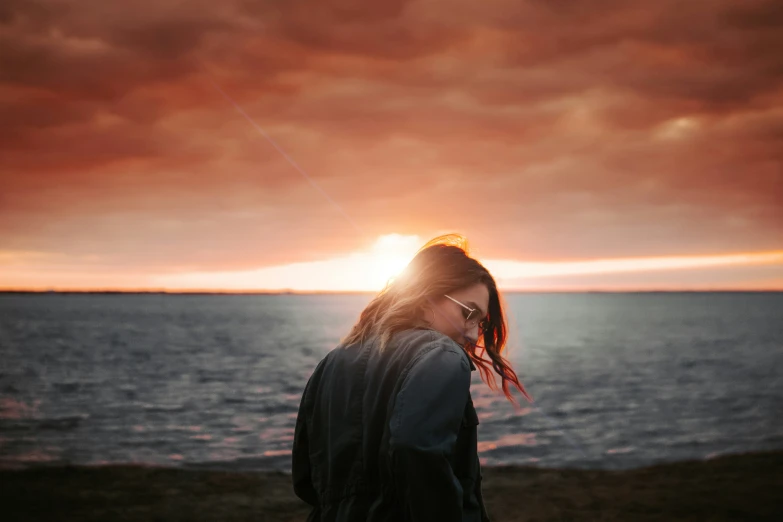 a woman standing on a rocky beach as the sun sets