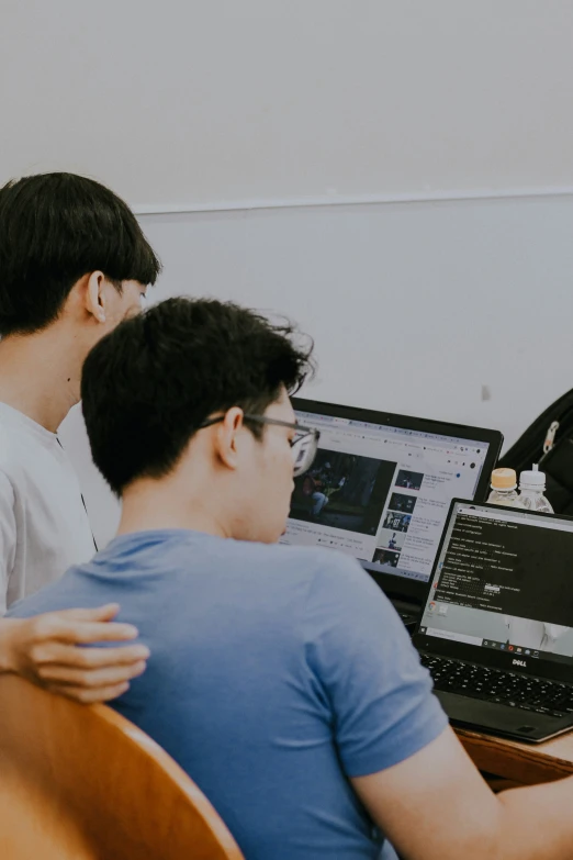 three young men sitting at a desk with two laptops on it