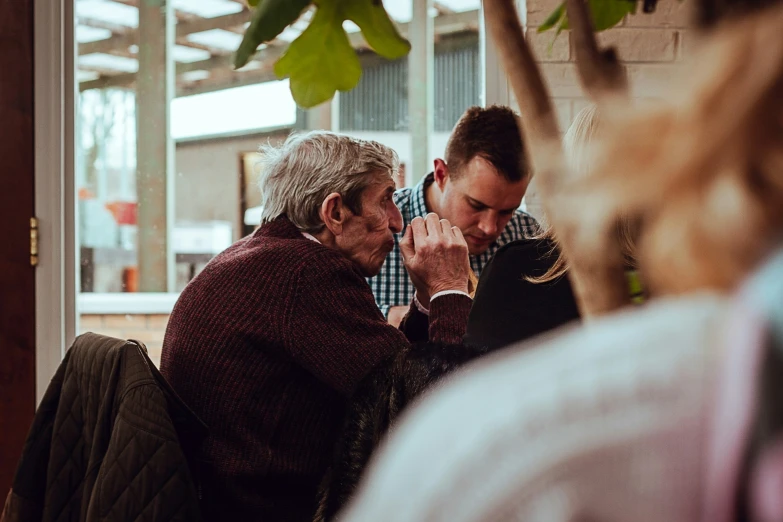 two men sitting at a table, one holding a cigarette