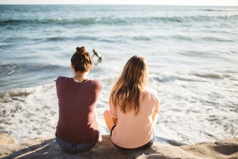 two people sitting by the water and looking at the beach