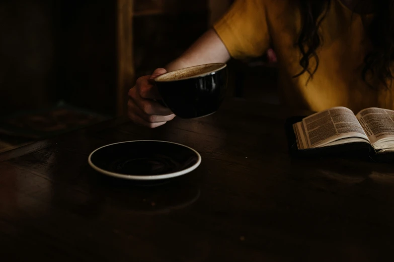 someone at a table with an open book holding a glass of liquid