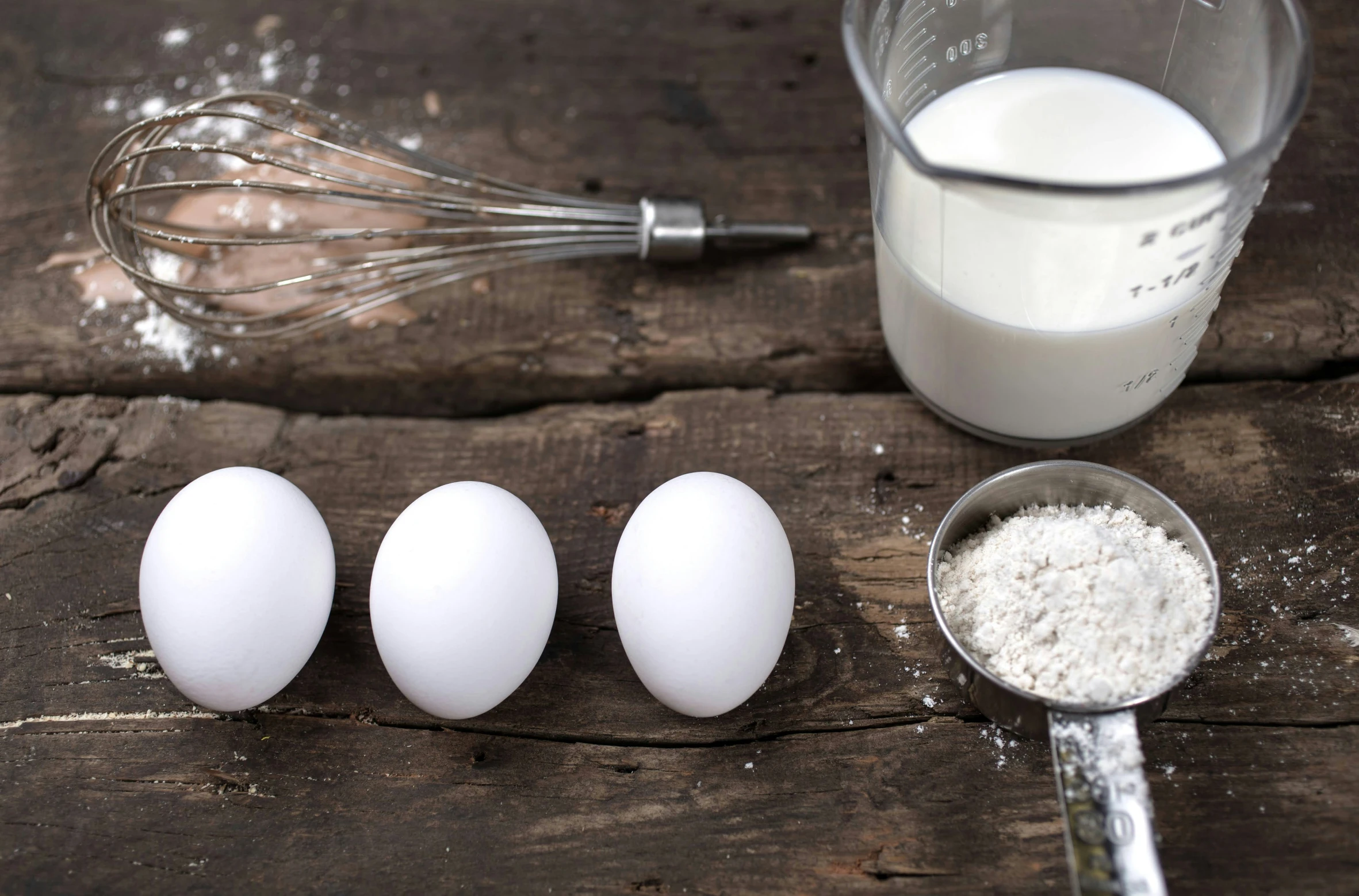 eggs being whisked in batter and next to glass and measuring spoon