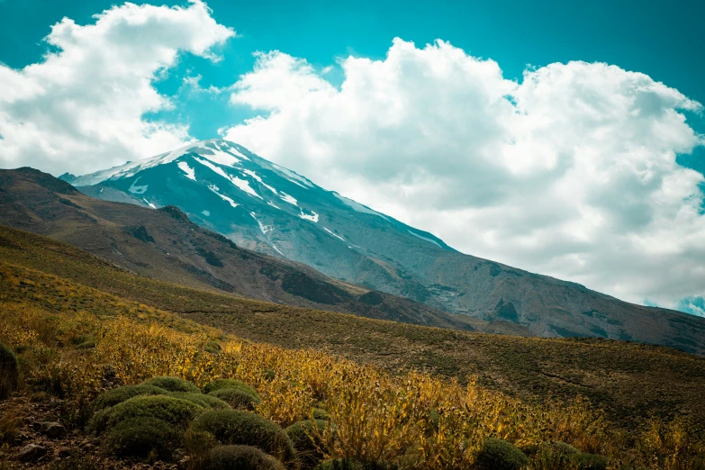 a mountain in the middle of a field with a blue sky and some clouds