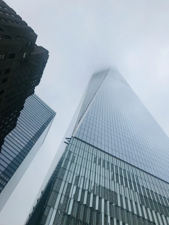 an upward view of two skyscrs with the clouds blowing in the air