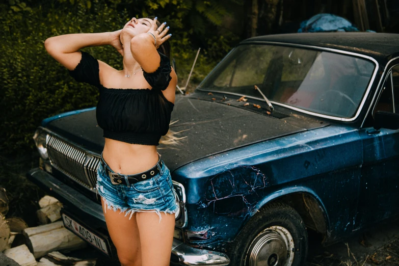 a woman in jean shorts leaning on the hood of an old fashioned pickup truck