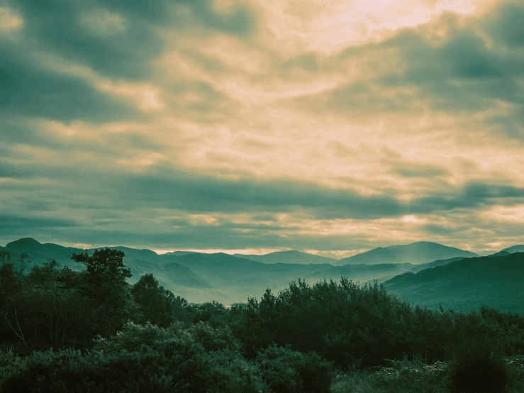 a mountain area with trees and mountains under a cloudy sky