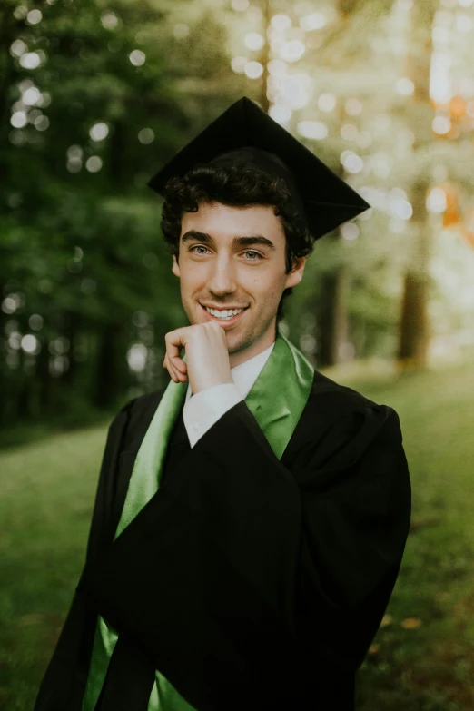 a male college graduate with his finger under his lip