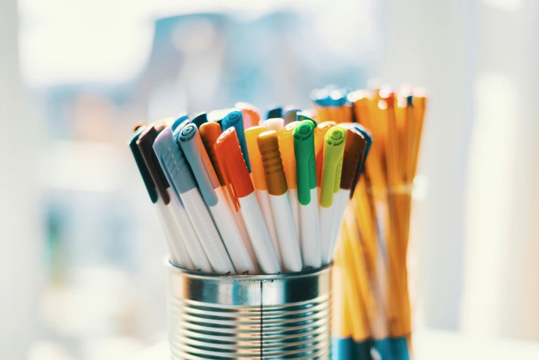 many colored pens in a tin on a table