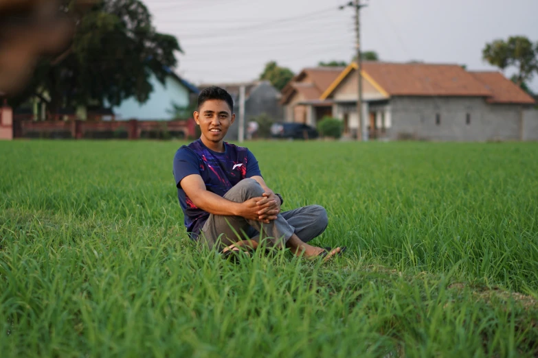 a young man sitting in a field with a dog on his lap