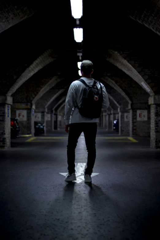 a skateboarder with a backpack standing alone in the dark