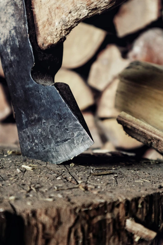 a shovel stuck in wood next to a stack of firewood