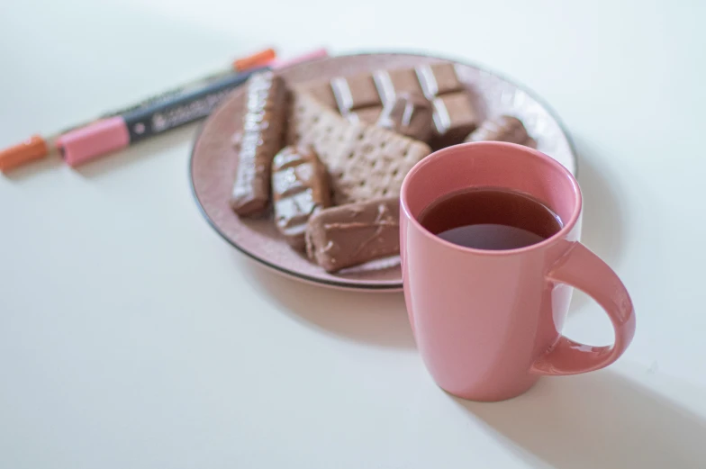 a pink cup sits in front of a plate with crayons