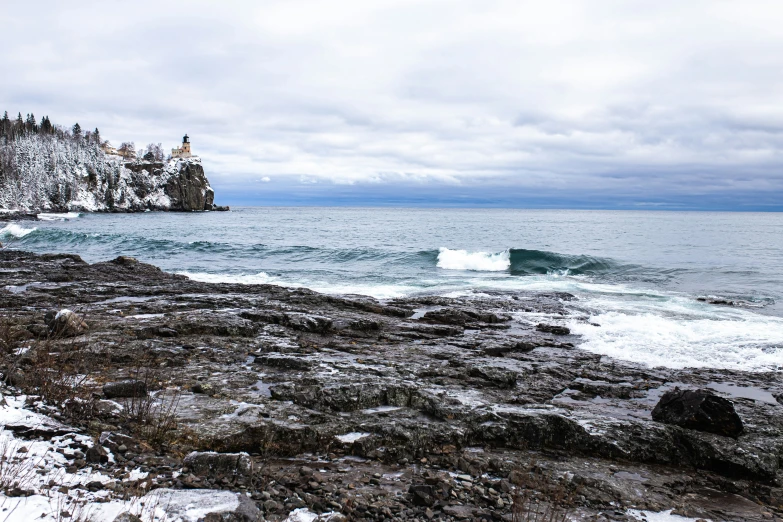 snow on the ground, rocks, and ocean in the foreground