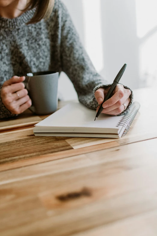 a woman sitting at a table with a notebook, pen and a cup of coffee