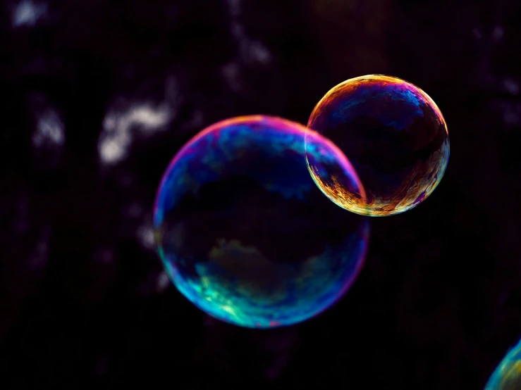 two bubble gums, one yellow and the other blue, blowing in a dark background