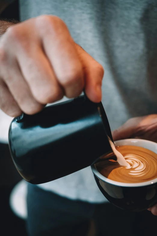 a person holding a cup of coffee while pouring milk