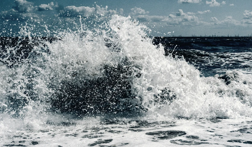 large wave crashing onto the beach with the sky in the background