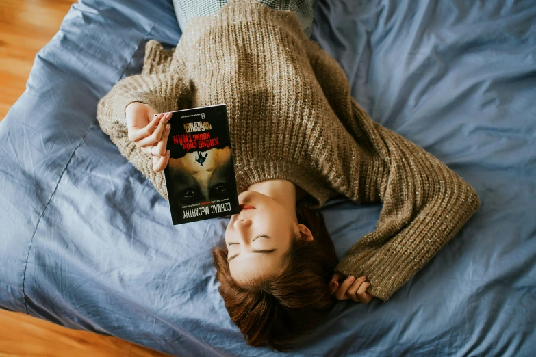 girl lays on a bed and reads a book in bed