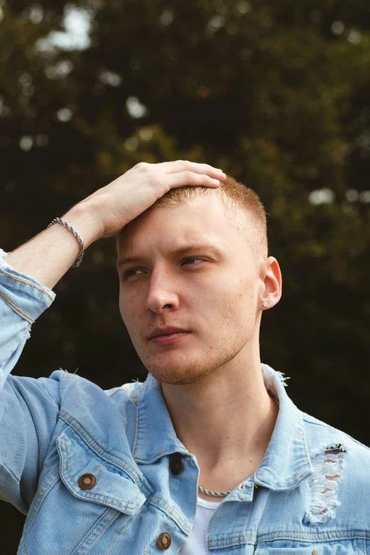 young man posing outdoors in blue jacket with trees behind him