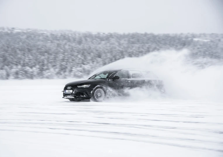 a black car driving through the snow in front of trees