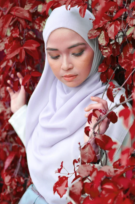 a woman standing under a tree filled with red leaves