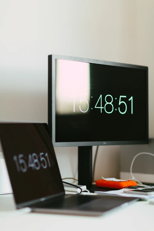 a black computer monitor displaying time on a white desk