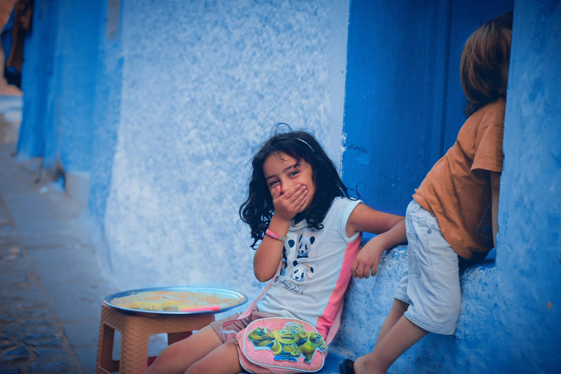 two children eating food outside on the blue wall