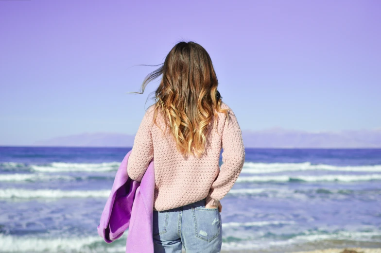 a girl in pink jacket looking out to sea from beach