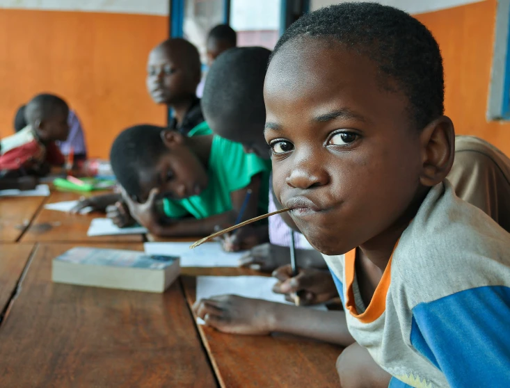 a school boy is holding up his toothbrush to his mouth in a classroom setting