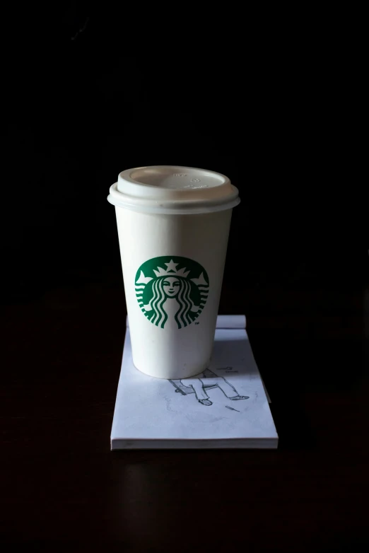 a starbucks cup on top of a notepad on a desk