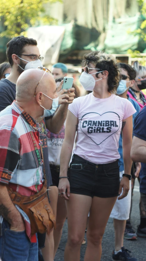 a person in shorts and a face mask looks at a person on their cell phone