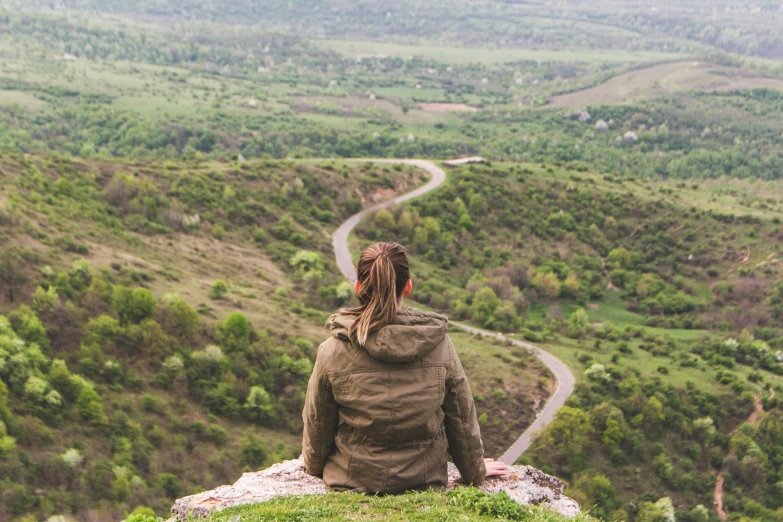 woman sitting down on hill overlooking winding road