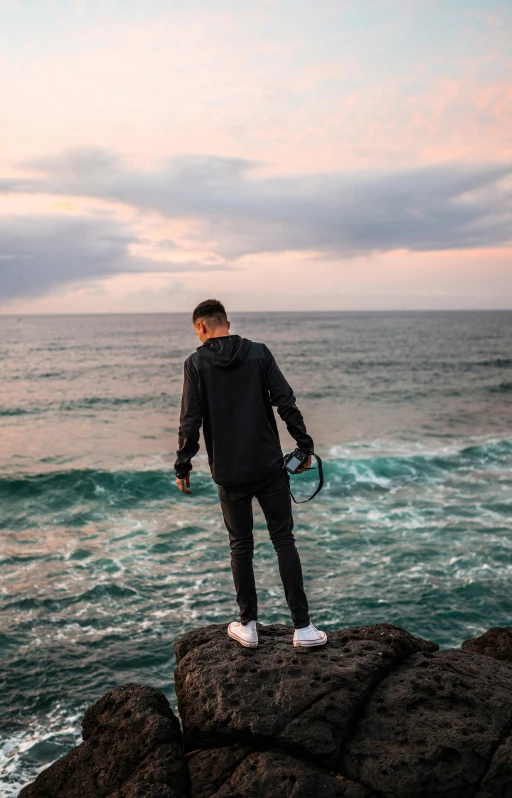 man standing on rock facing ocean looking off into the distance