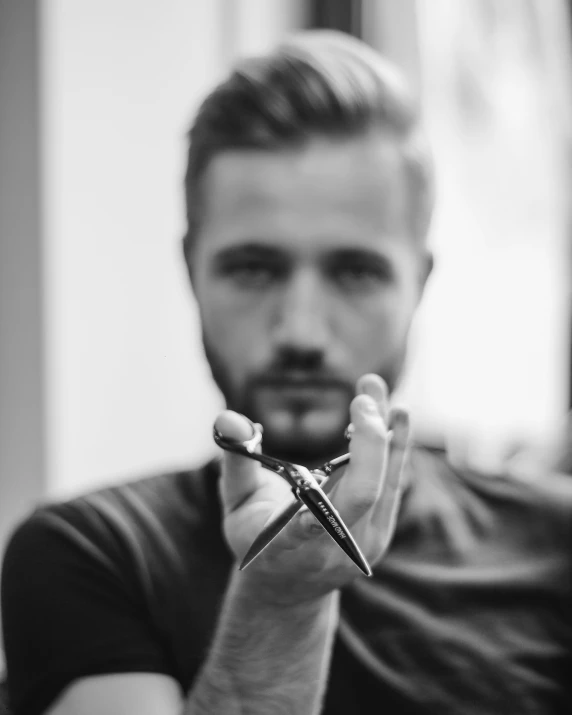 a young man in a short black shirt holds a small pair of scissors