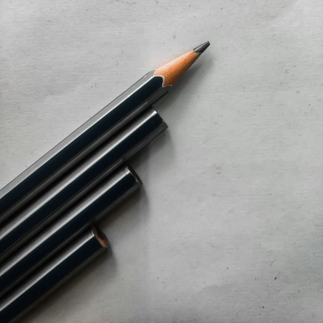 a brown pencil and four black pens are on a white surface