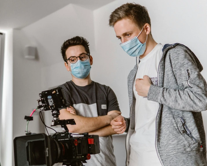 two men in face masks and a camera on the film set