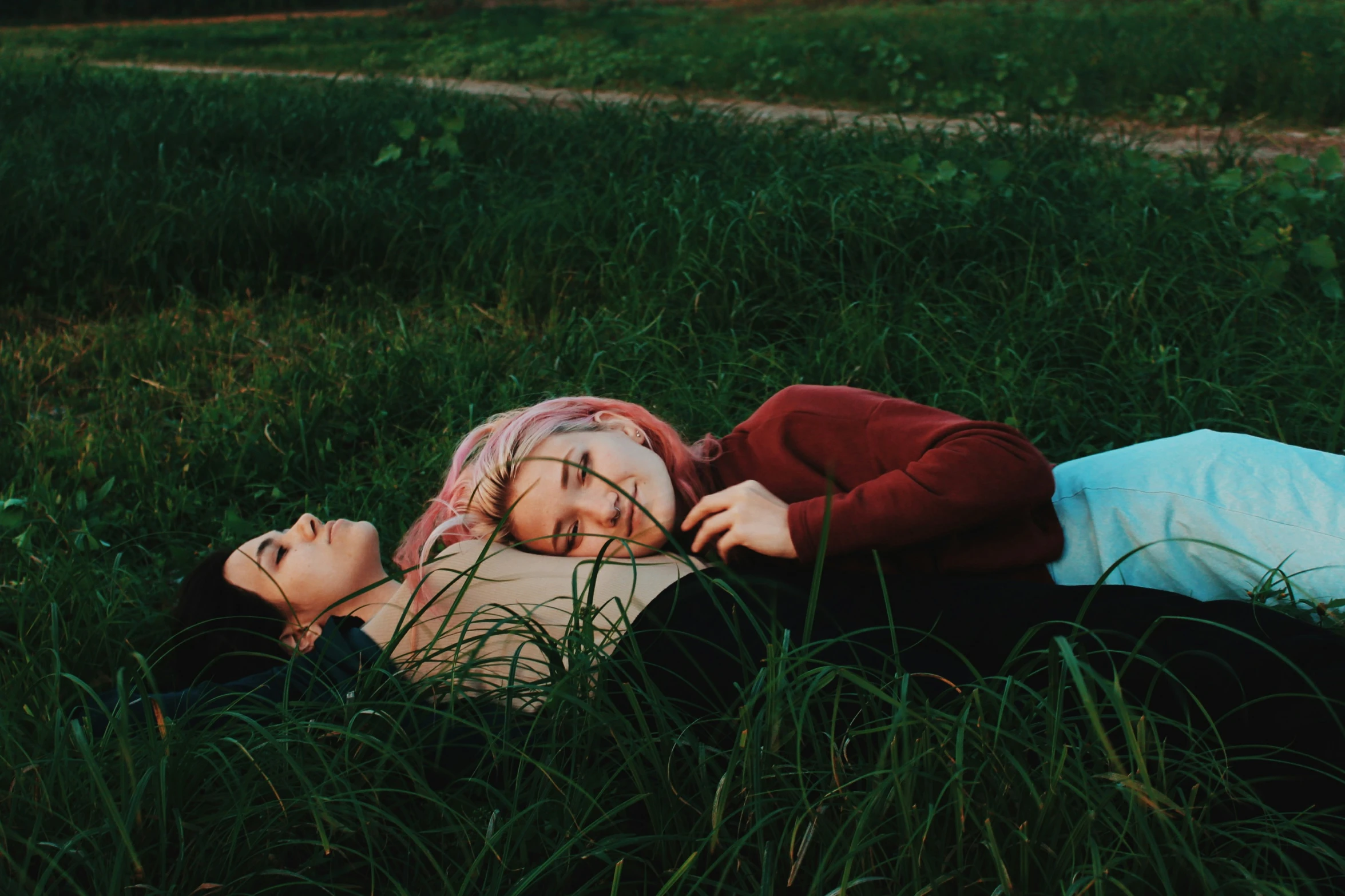 a young couple laying in grass one holds the head of another