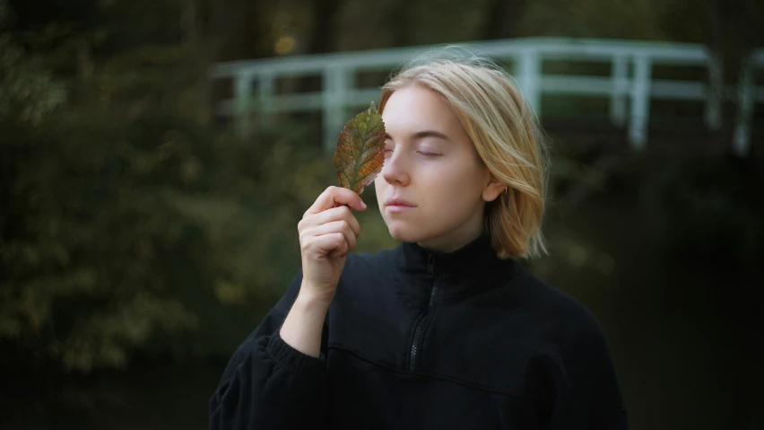 a woman holding a leaf with her eyes closed