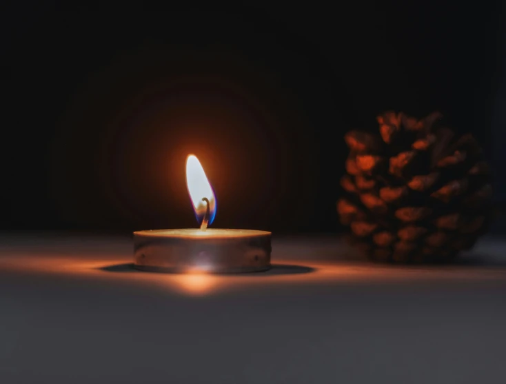 a lit candle with small pine cones nearby