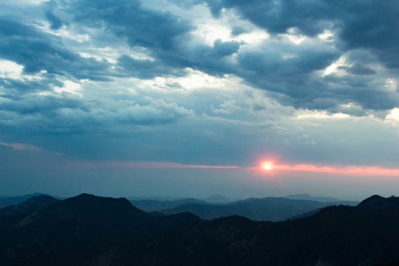 the sun rises in the clouds above the mountains