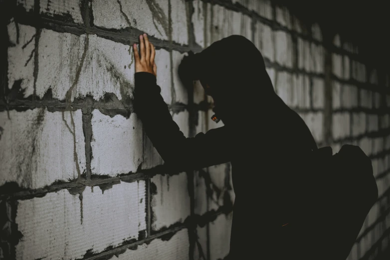 a person in a hooded jacket holding their hand against a wall