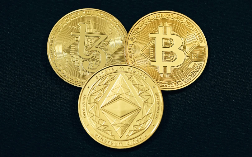 three gold bitcoins with different symbols on the top of one coin