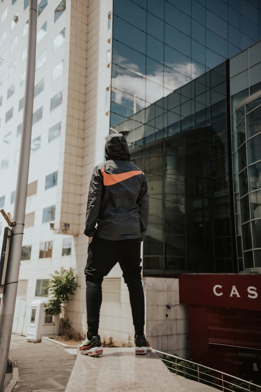 man in black jacket, jeans and orange vest outside office building