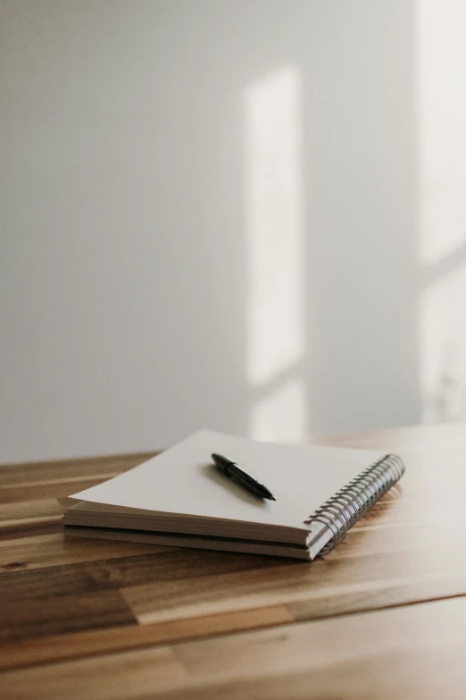 notebook on a table next to a window with white walls