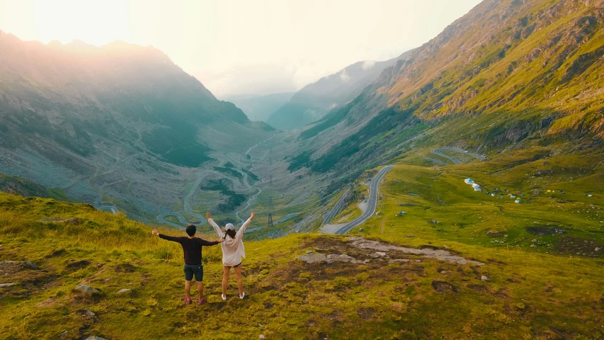 two people are on a mountaintop with their arms in the air