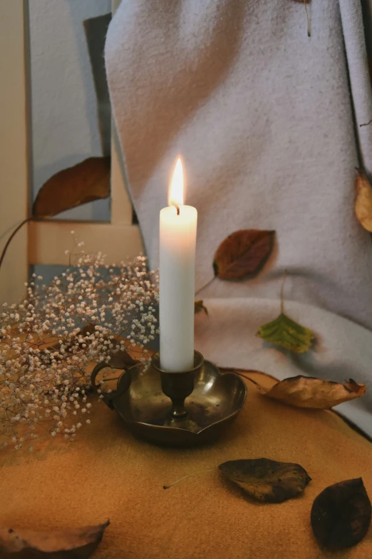 the candle is sitting on a table with leaves around it